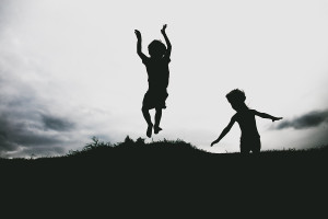 Silhouettes of kids jumping from a sand cliff at the beach